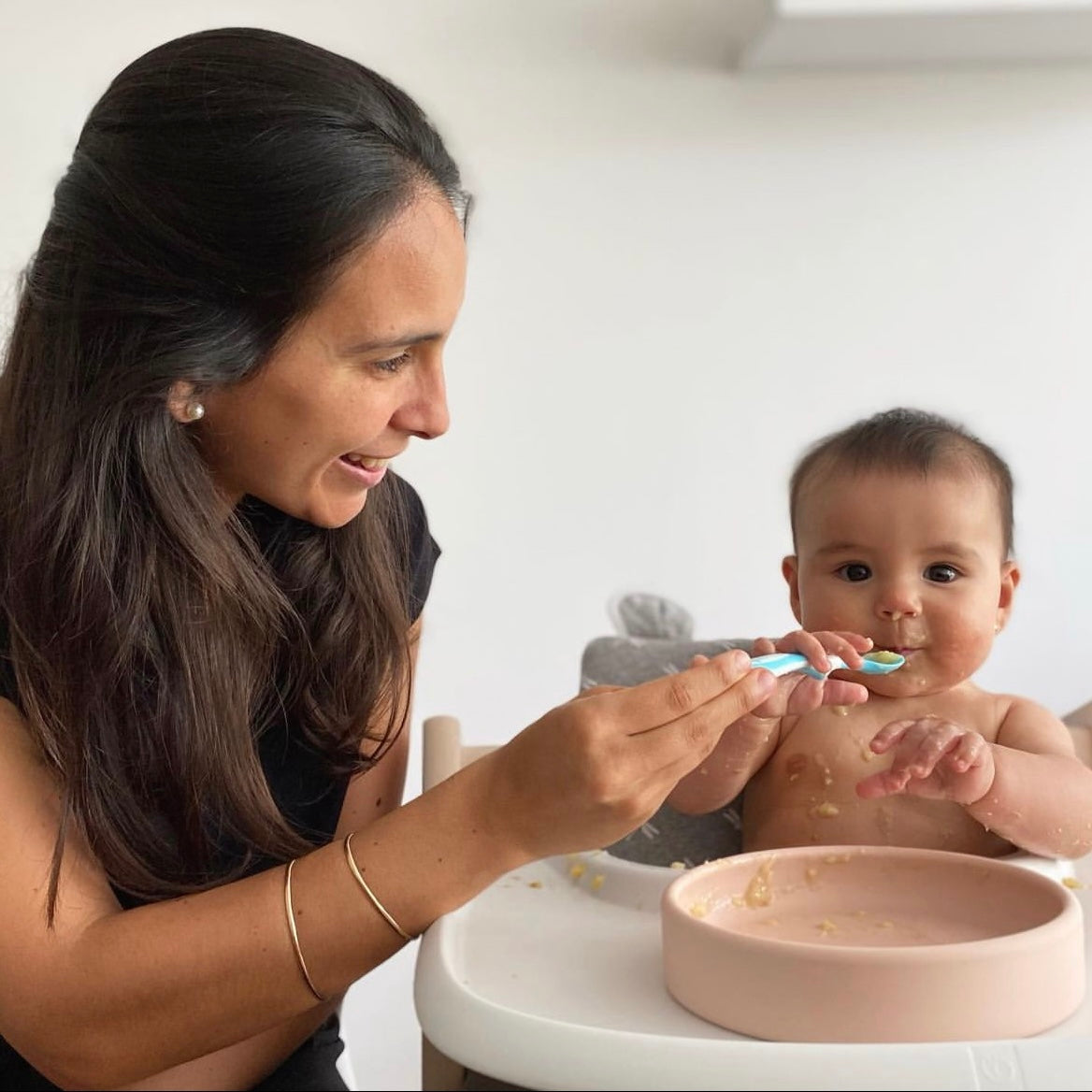 mom feeding her baby from a blush aplainr silicone plate on a stokke high chair